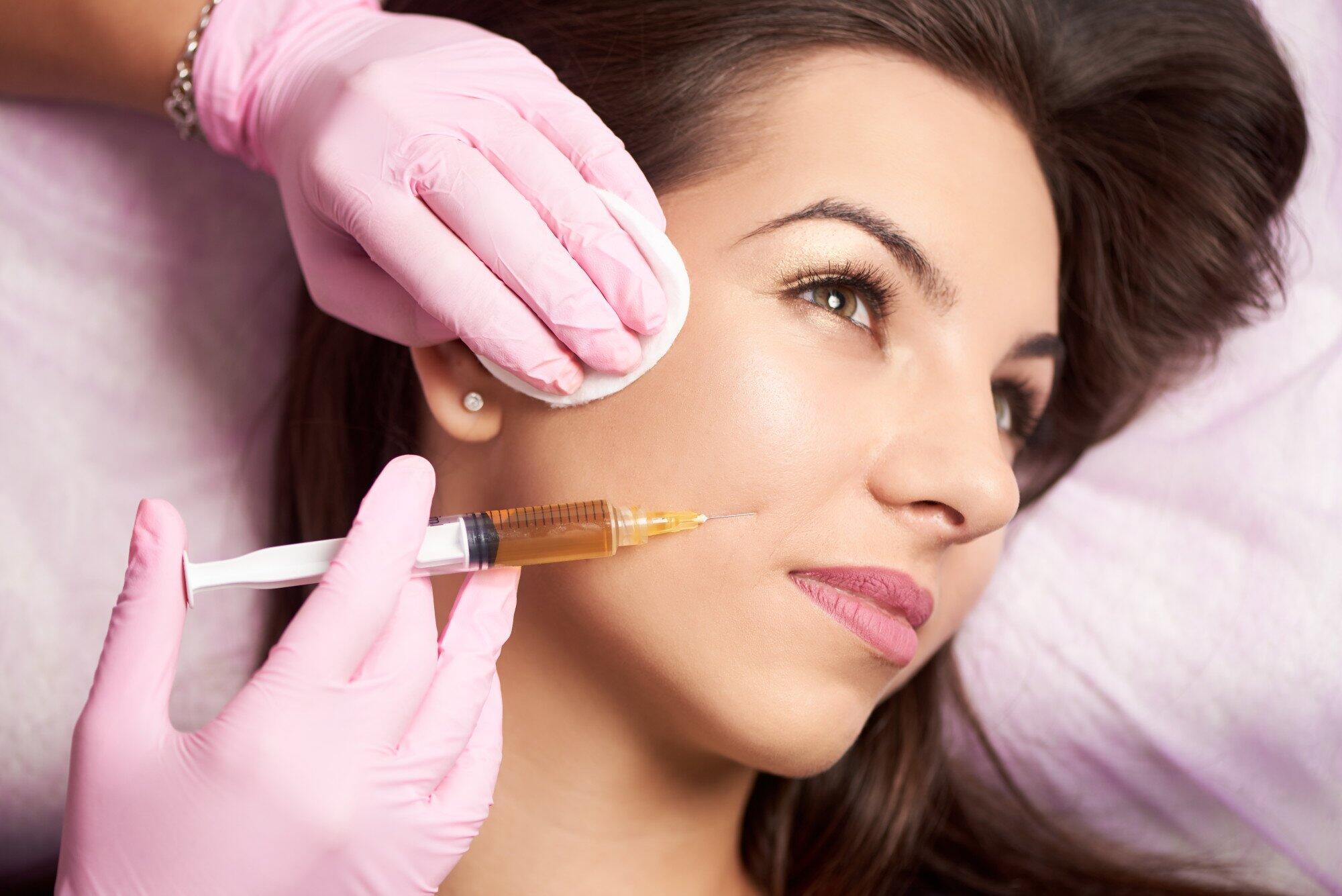 Close-up of beautiful woman getting injection in the cosmetology salon. Doctor in medical gloves with syringe injects cheeks drug